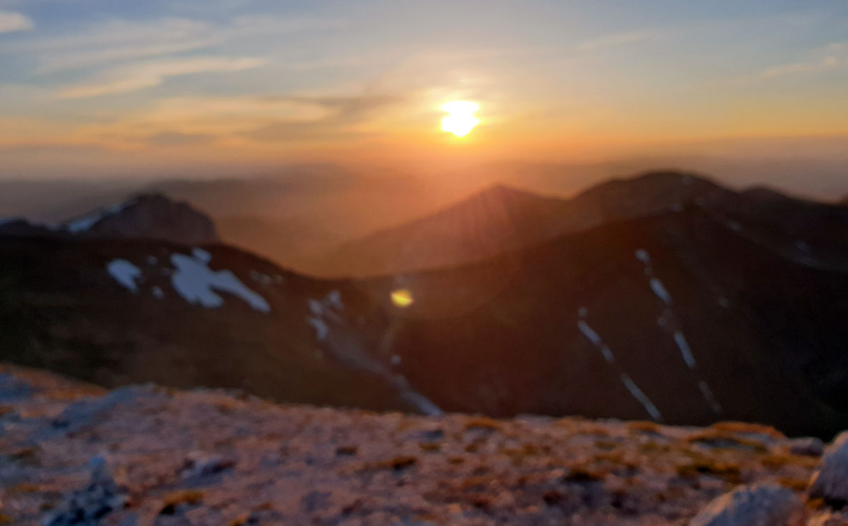 Una veduta panoramica dalla vetta del Monte Priora con il sole che tramonta dietro alla Croce di Monte Rotondo, nel Parco Nazionale dei Monti Sibillini